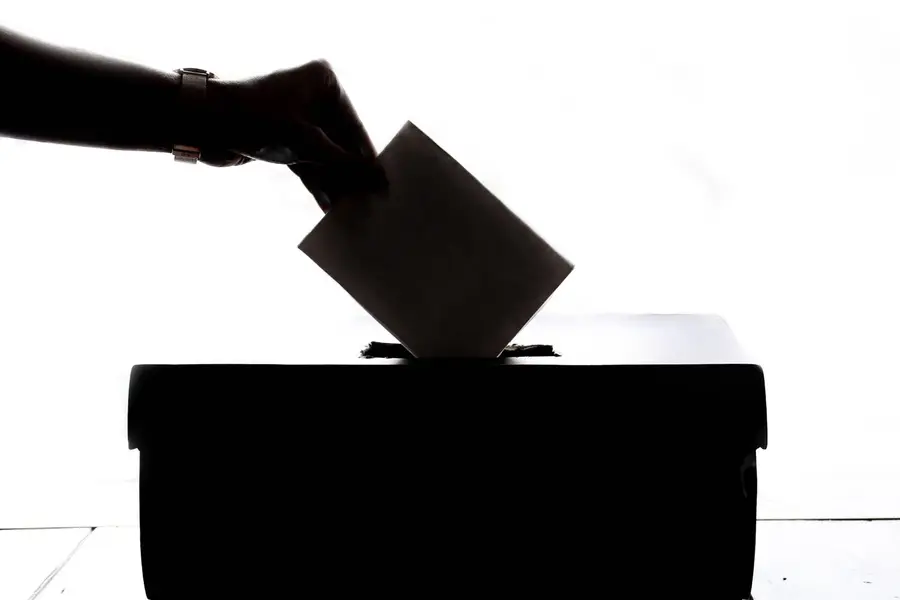 A hand placing a ballot in a box